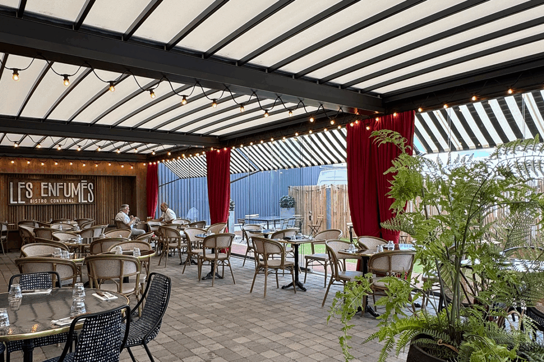 Pergola à toit rétractable avec parois vitrées en façade, stores bannette à projection, rideaux classement au feu M1 et guirlande LED installée au restaurant Les Enfumés à Montbert (44) par ESPACIO